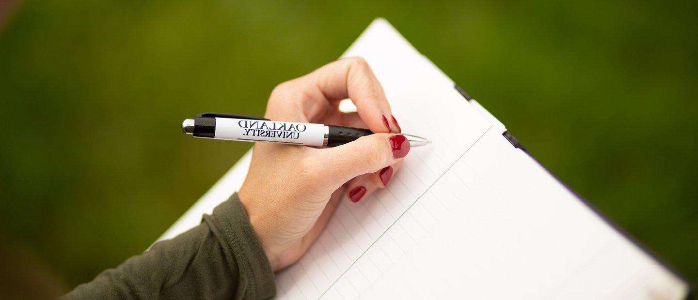 Closeup of hand holding a pen writing in a notebook.